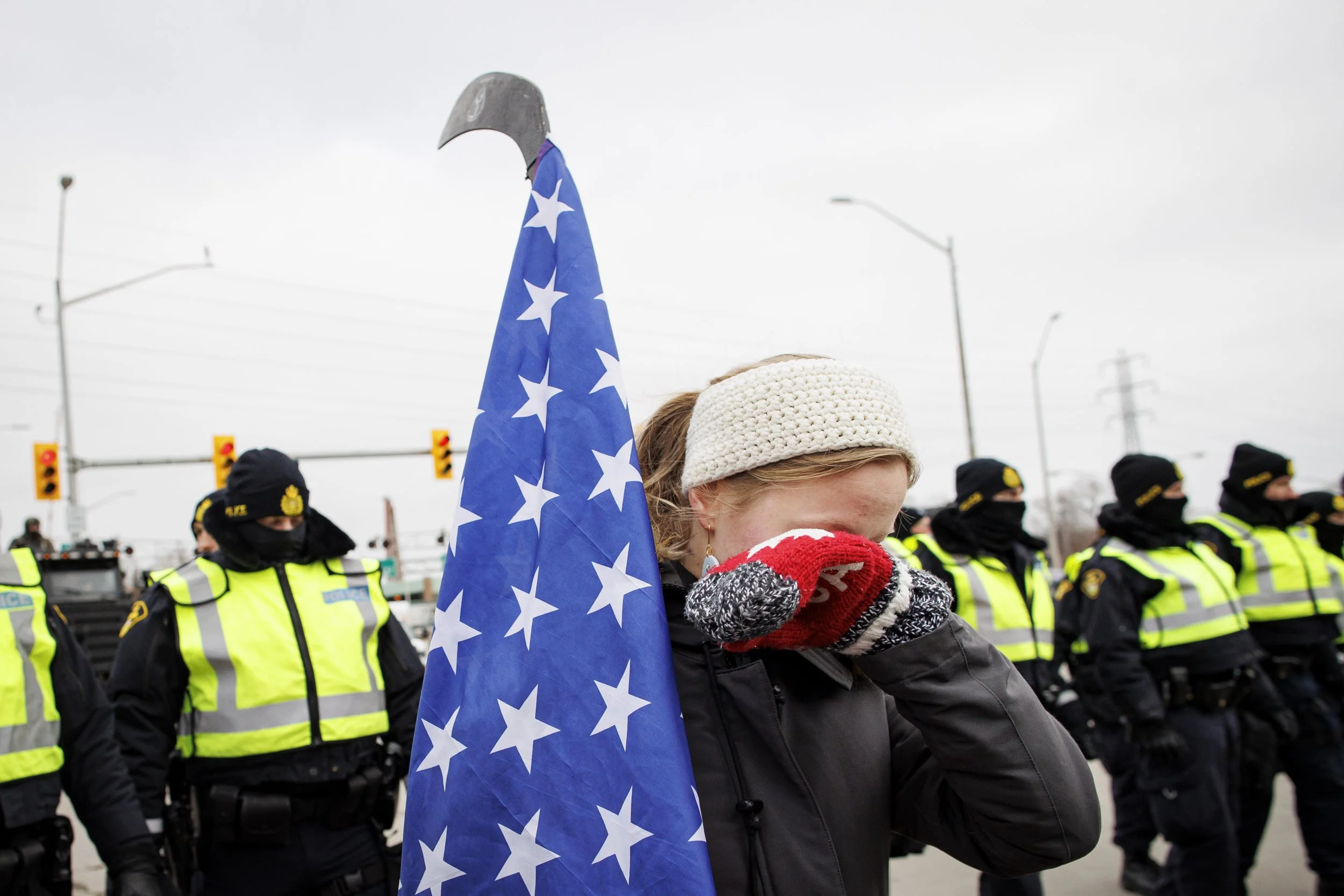 An anti-mandate protester carrying an American flag cries as police officers clear the Ambassador Bridge blockade, in Windsor, Ont., on Feb. 12, 2022.