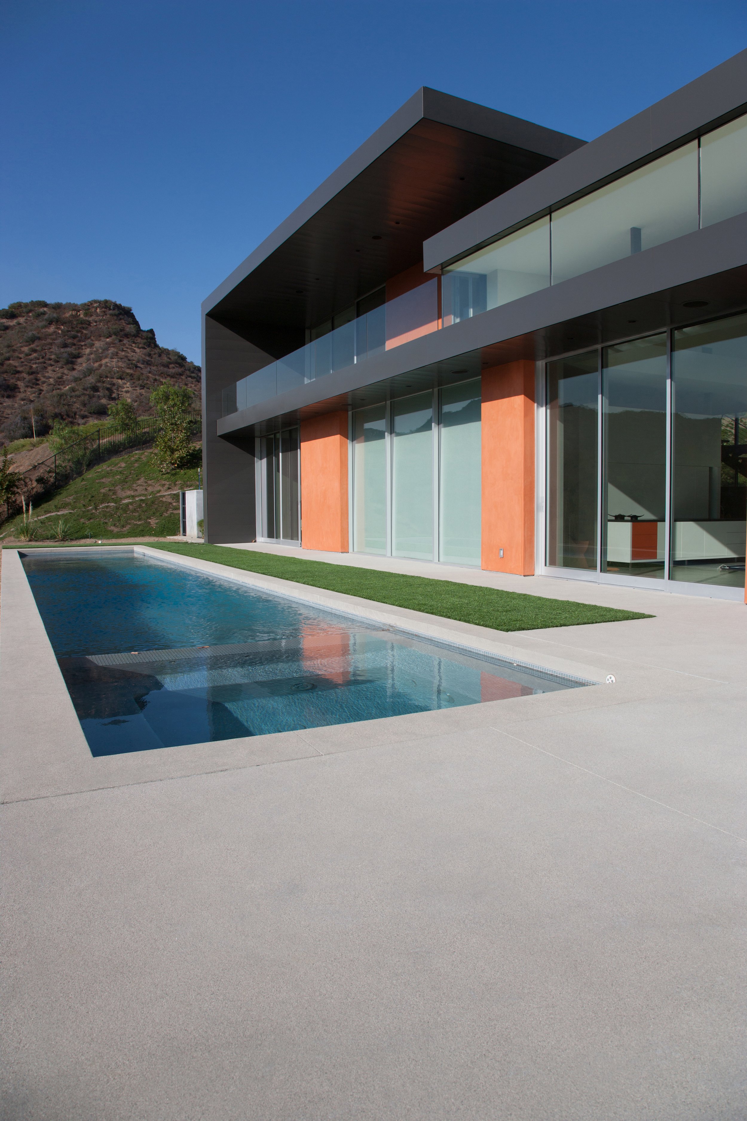 Modern house with large glass windows, a swimming pool, and a hillside in the background.
