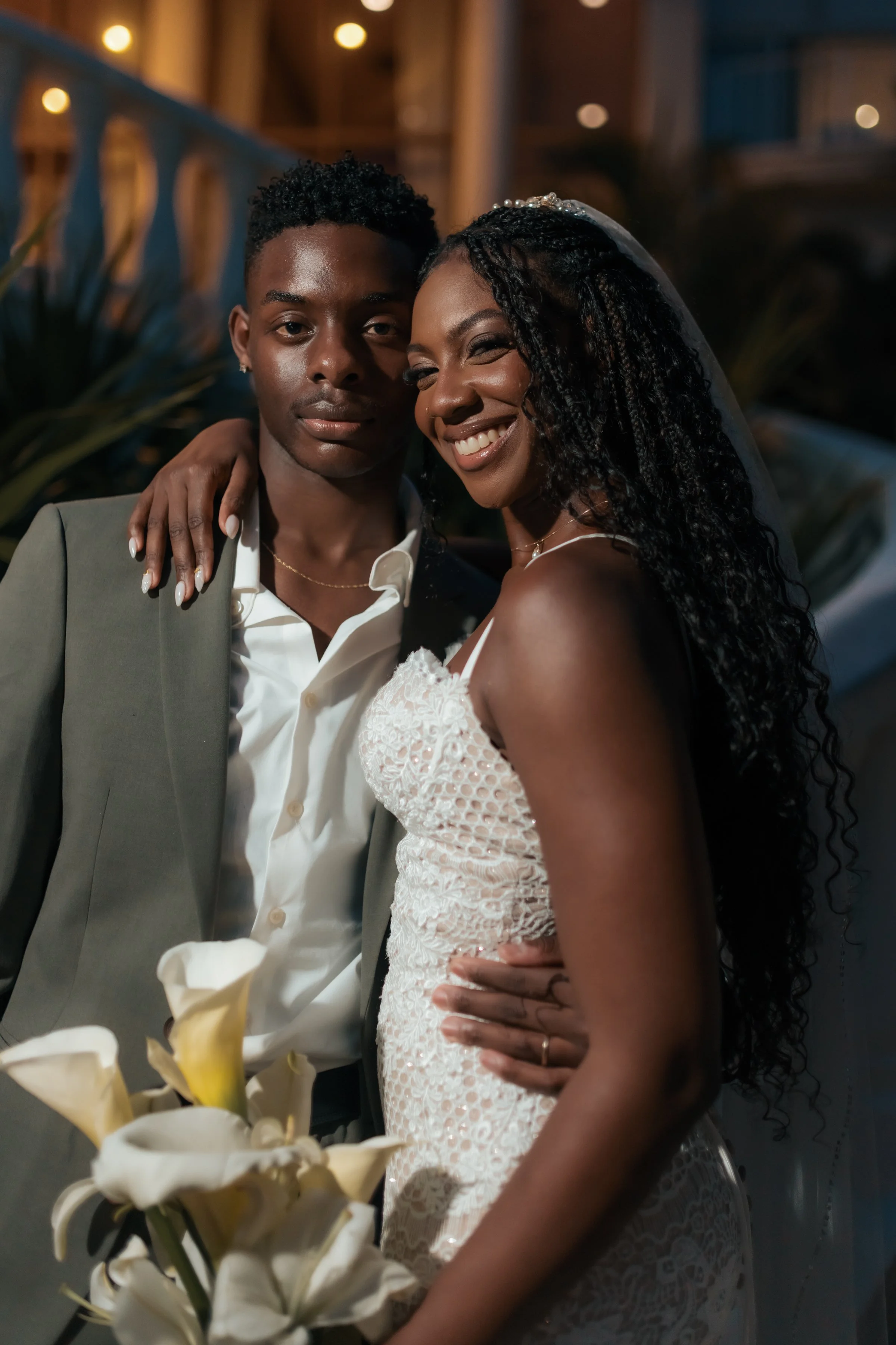 A joyful bride and groom pose closely together at their wedding, with the bride smiling and holding a bouquet of white calla lilies.