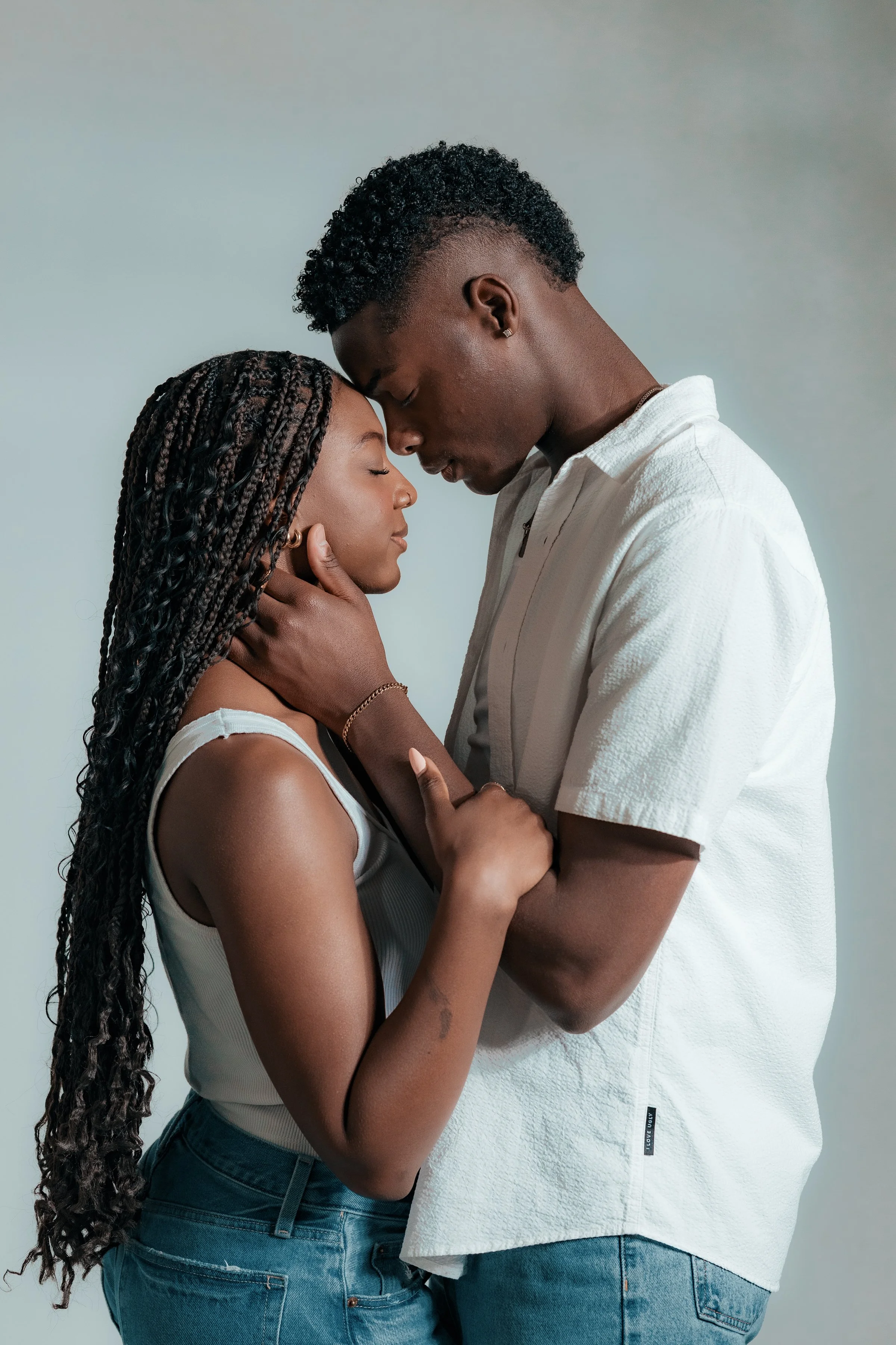 A couple sharing an intimate moment, standing close with their foreheads touching and eyes closed.