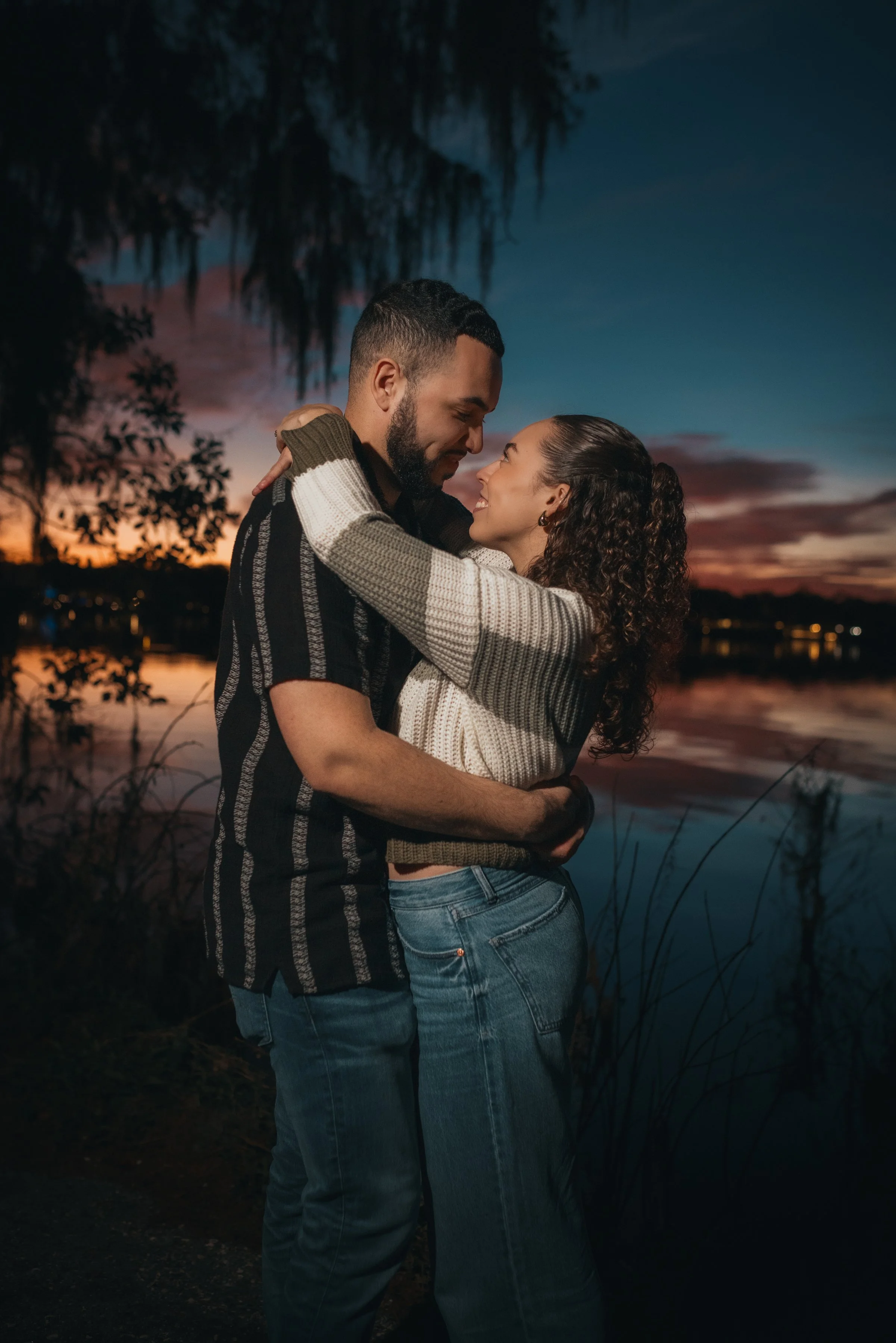 A couple sharing a romantic embrace at sunset near a body of water.