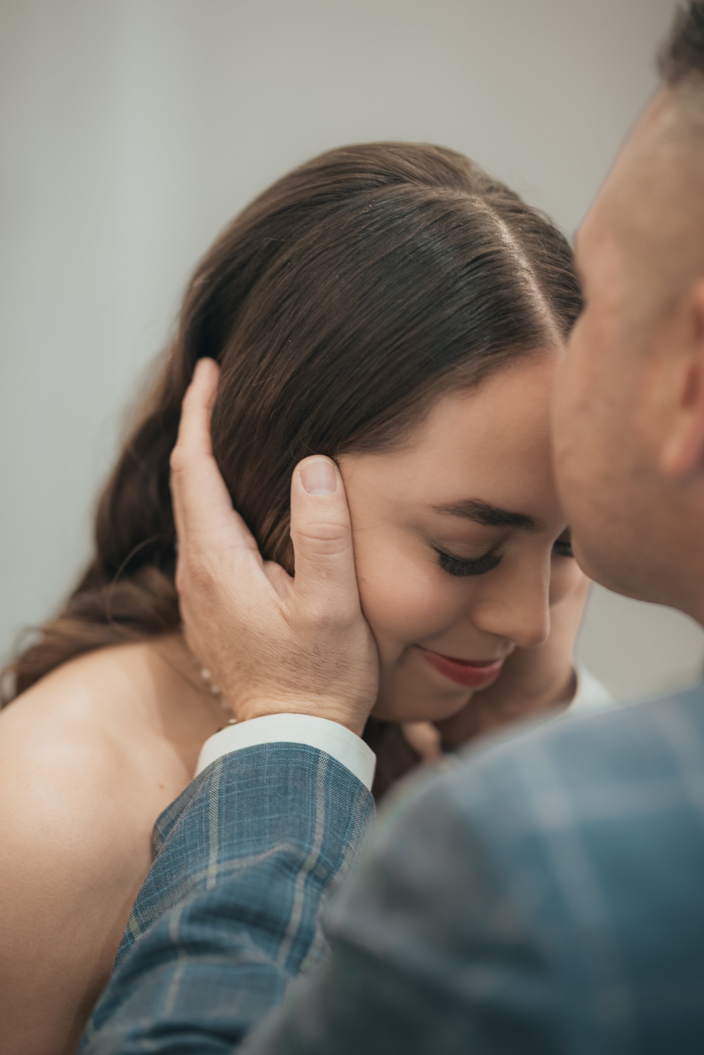 A couple sharing an intimate moment, with the man gently holding the woman’s face as they lean in close, eyes closed, during a wedding or special occasion.
