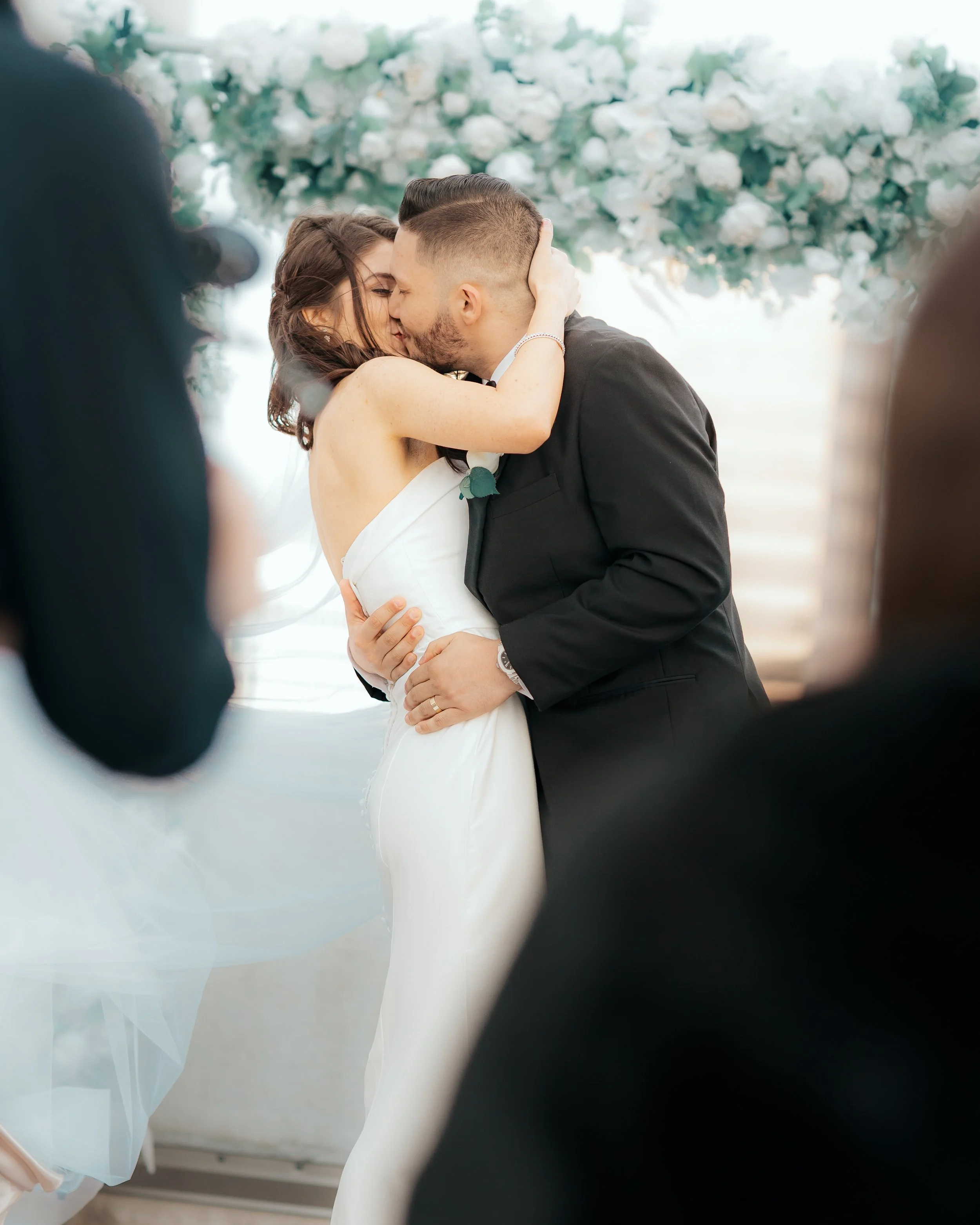 Bride and groom kissing during their wedding ceremony, surrounded by guests.