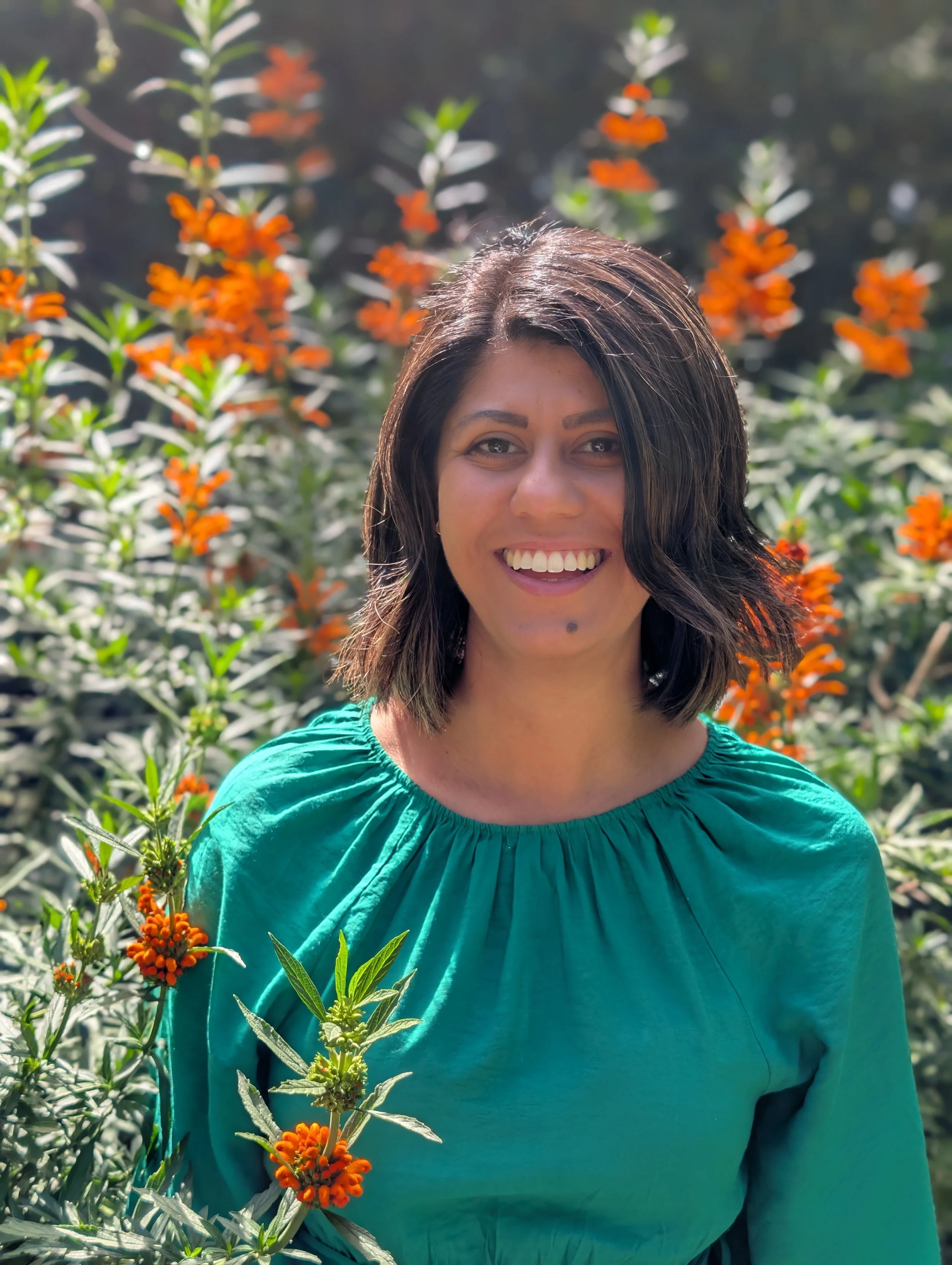 A person dressed in green surrounded by a field of blooming orange flowers.