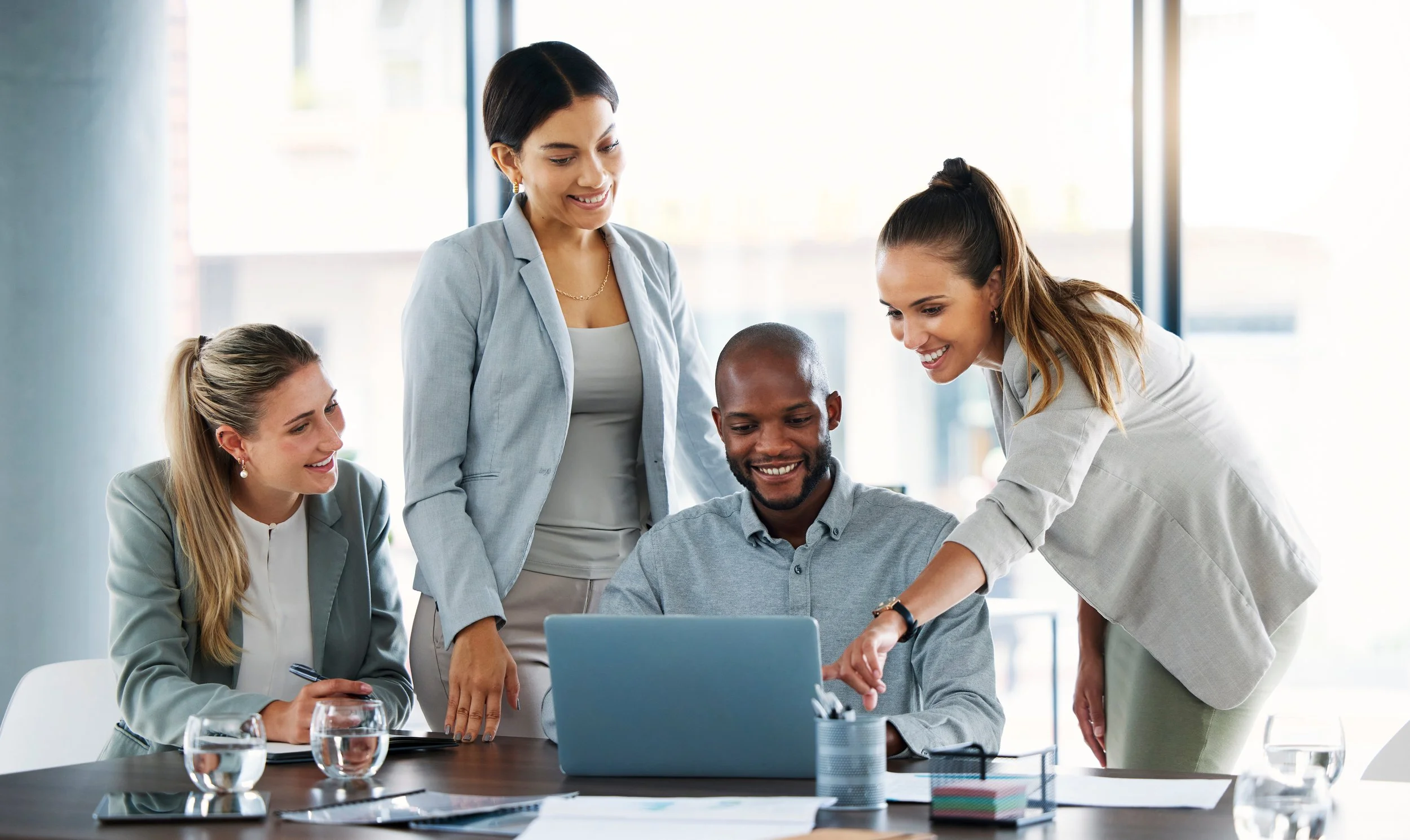 Enterprise wide modernization effort show a diverse group of five professionals gathered around a laptop in a modern office, collaborating and smiling.