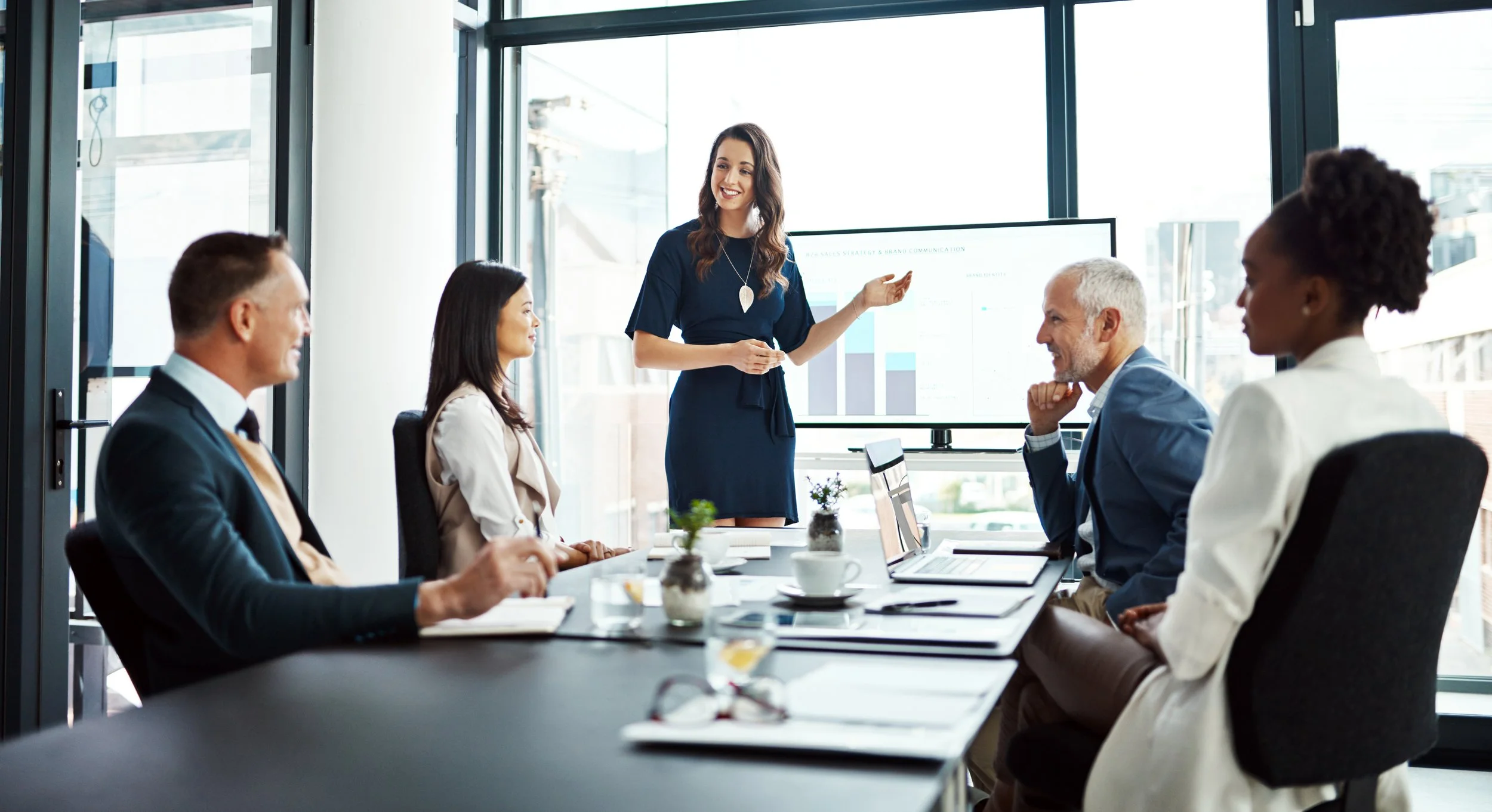 Women and men in business attire attending a demo presentation to a group of executives.
