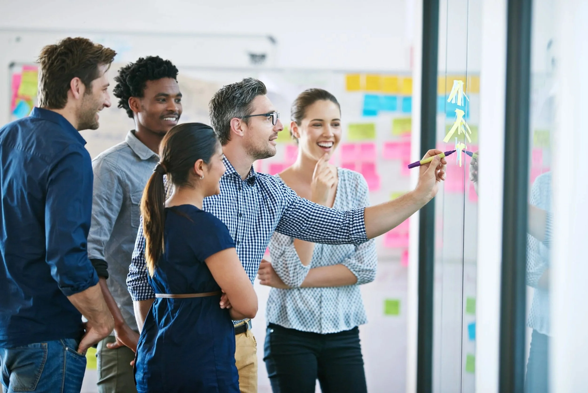 Modernization begins with the users and business organizations involved and here is diverse people standing in front of a glass wall, engaging in a brainstorming or collaborative work session.