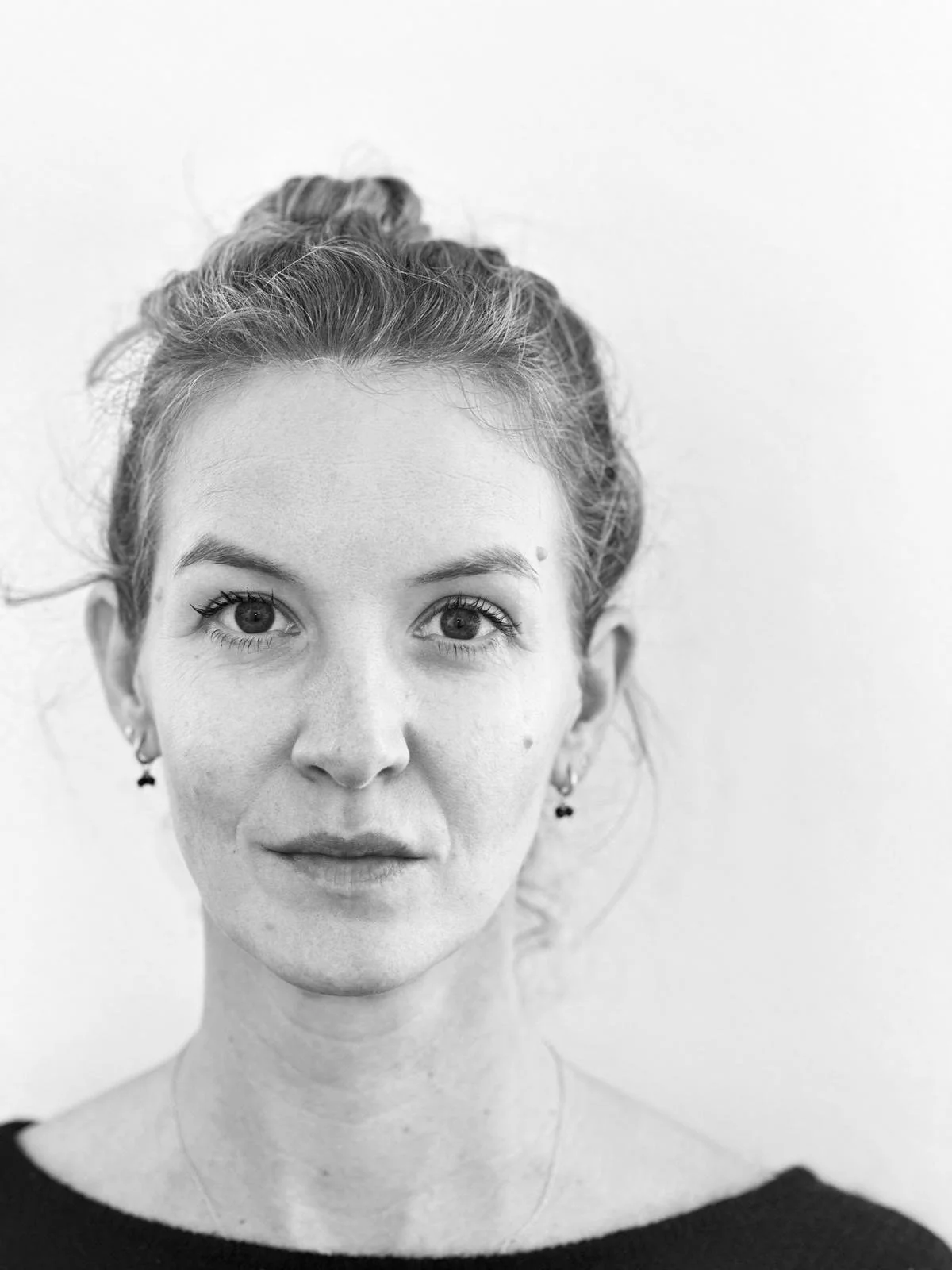 Black and white portrait of a woman with light skin, red hair tied up, and earrings, looking directly at the camera with a neutral expression.