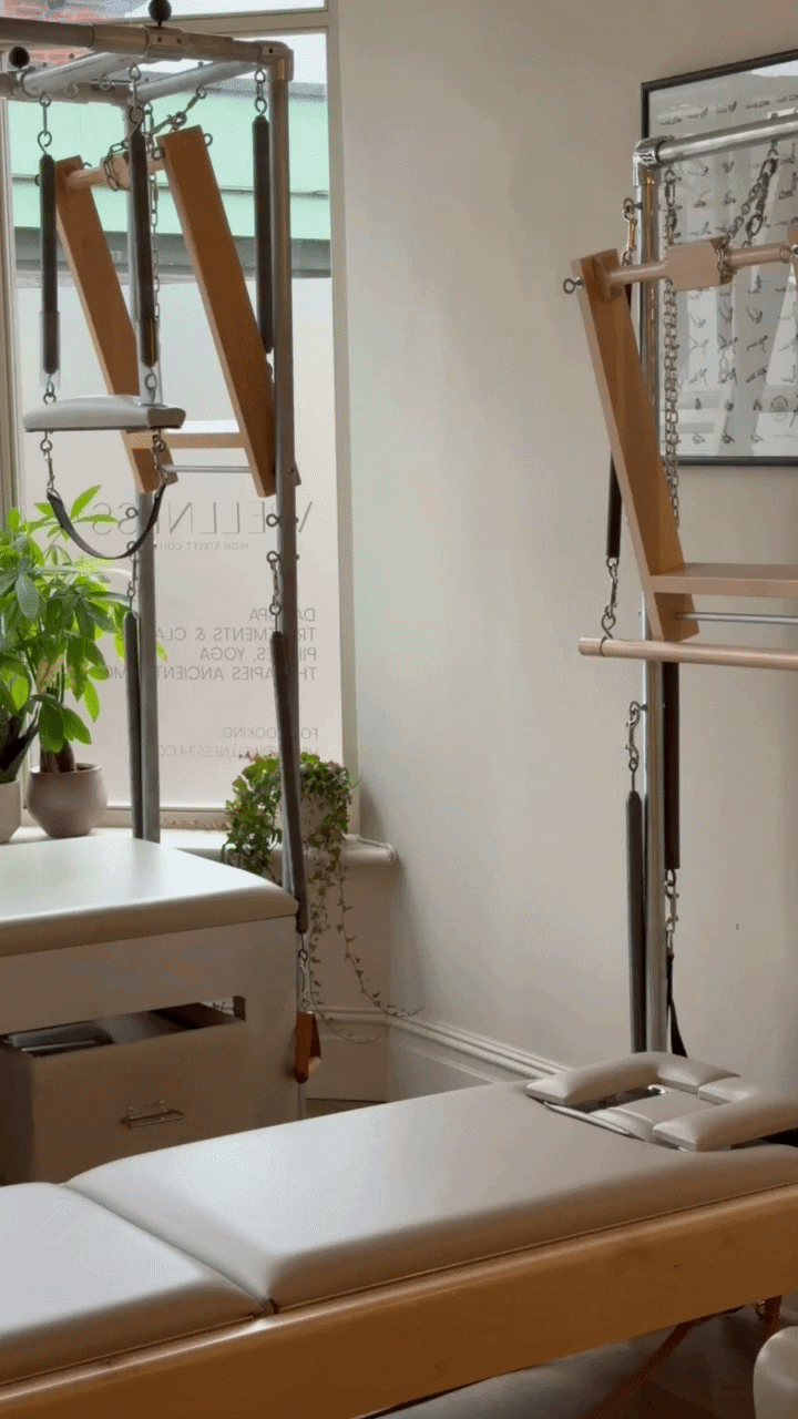 Pilates studio with reformer machines, potted plants, and a window with frosted glass.