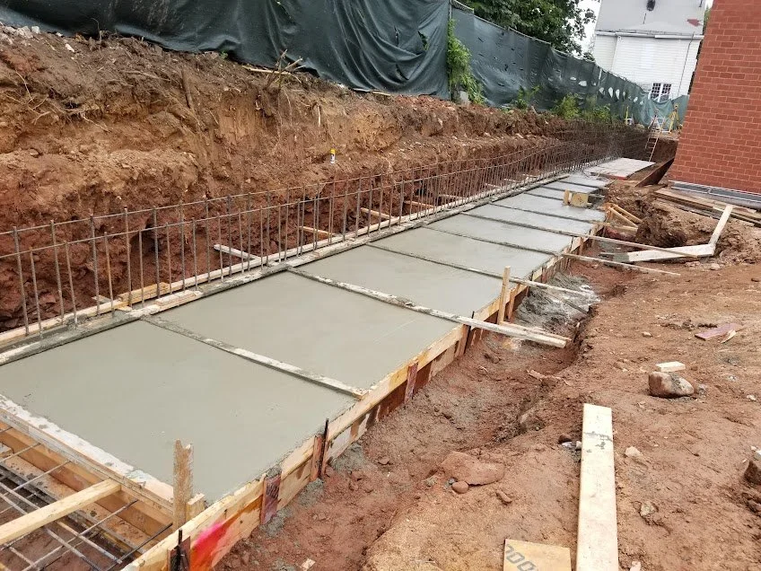Concrete sidewalk or foundation being poured and smoothed on a construction site with wooden and metal forms in place.