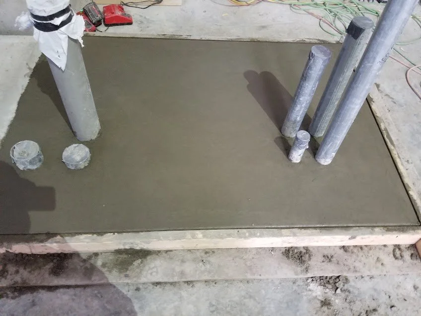 Concrete floor with several metal pipes, some vertical and some covered, at a construction site.