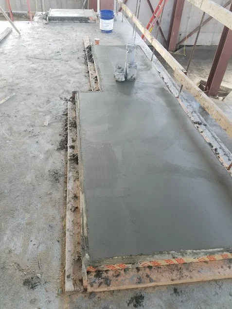 Freshly poured concrete slab on a construction site with wooden framing and scaffolding.