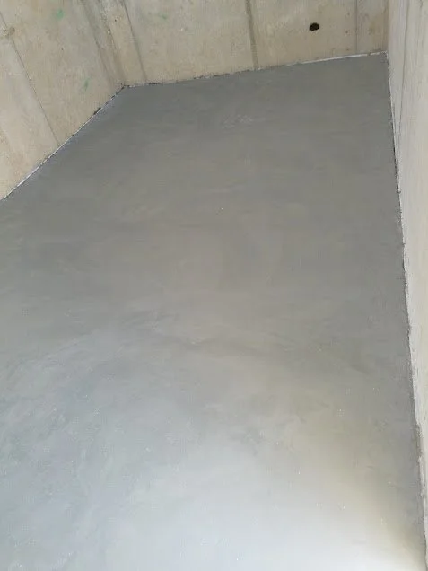 A corner of a room with concrete walls and a newly poured concrete floor.