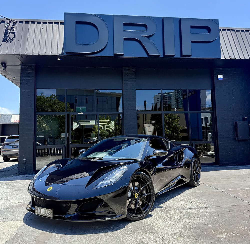 Black sports car parked outside a building with a large 'DRIP' sign on the facade.