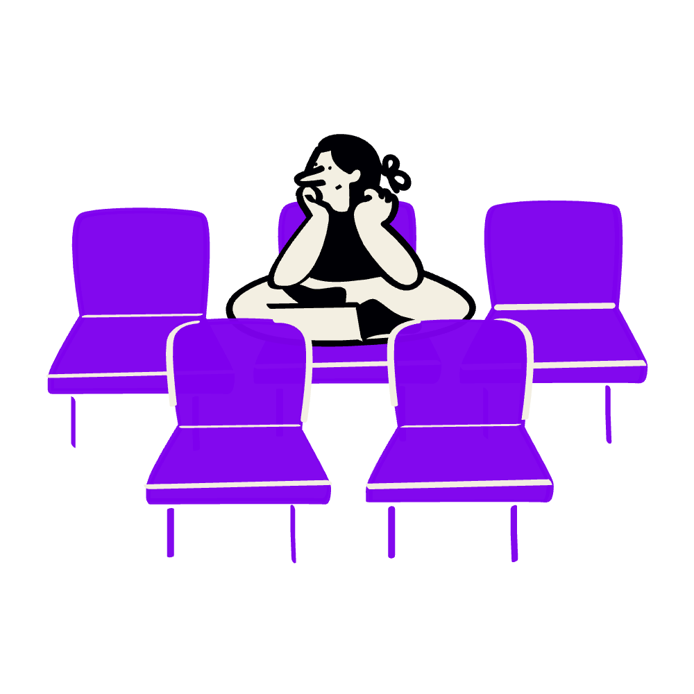 A woman sitting alone at a table with five purple chairs around her, appearing thoughtful or sad.
