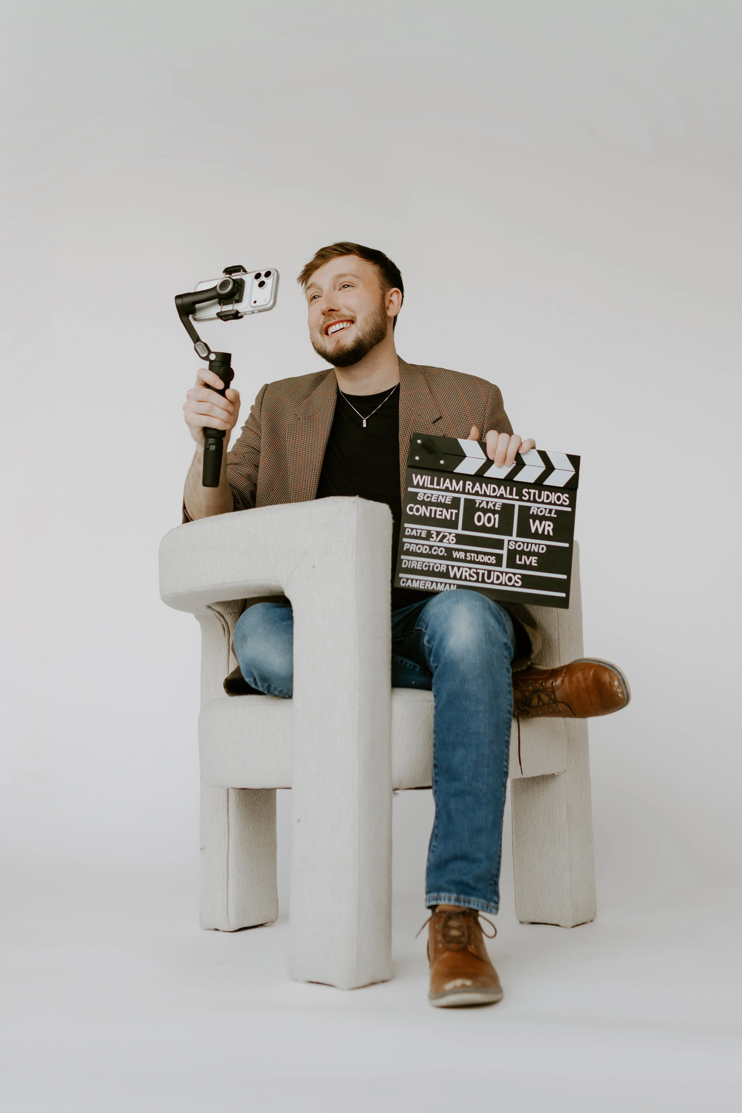 William Randall holding a camera setup and clapperboard while seated during a content shoot.