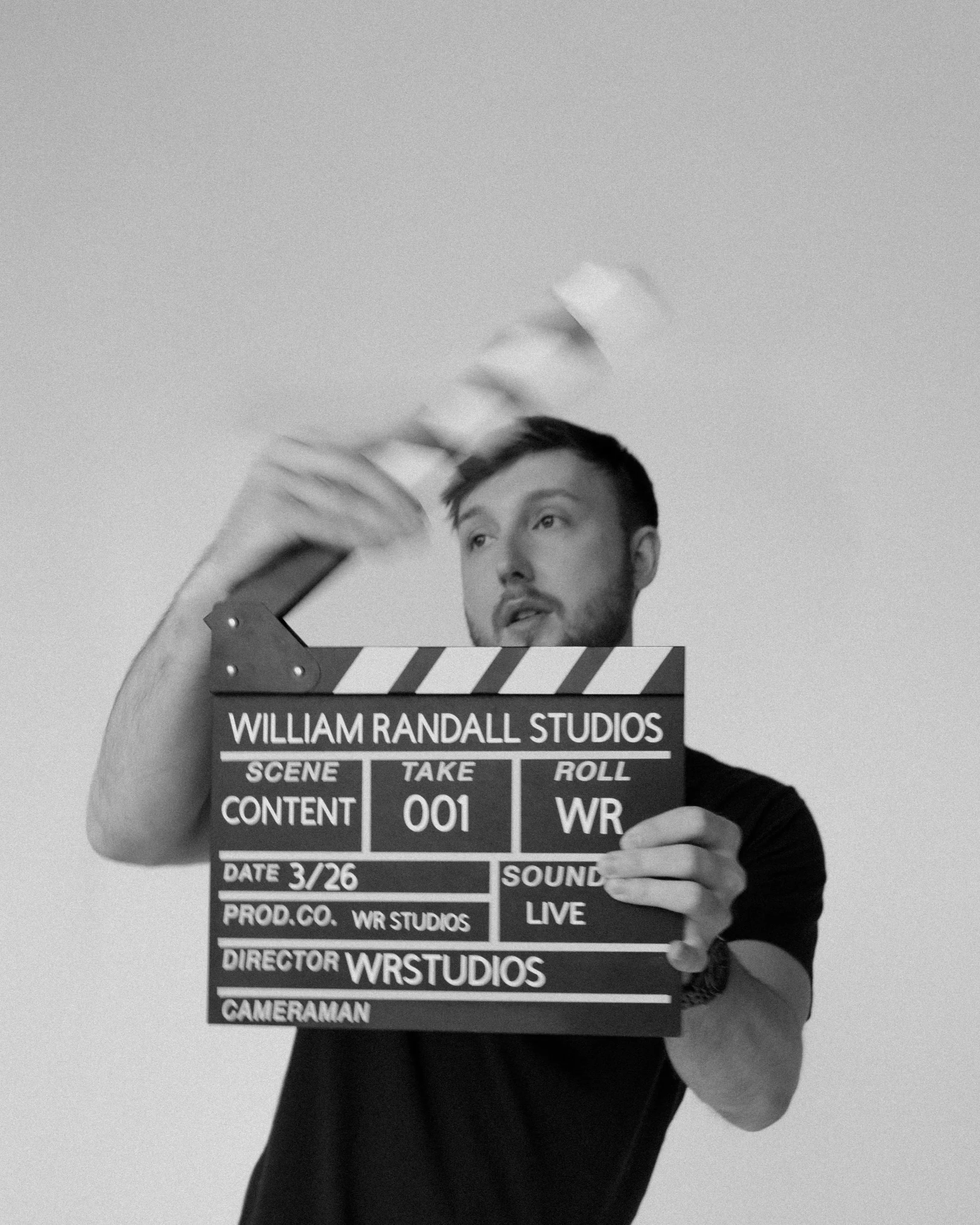 William Randall holding a clapperboard mid-motion during a content shoot in black and white.