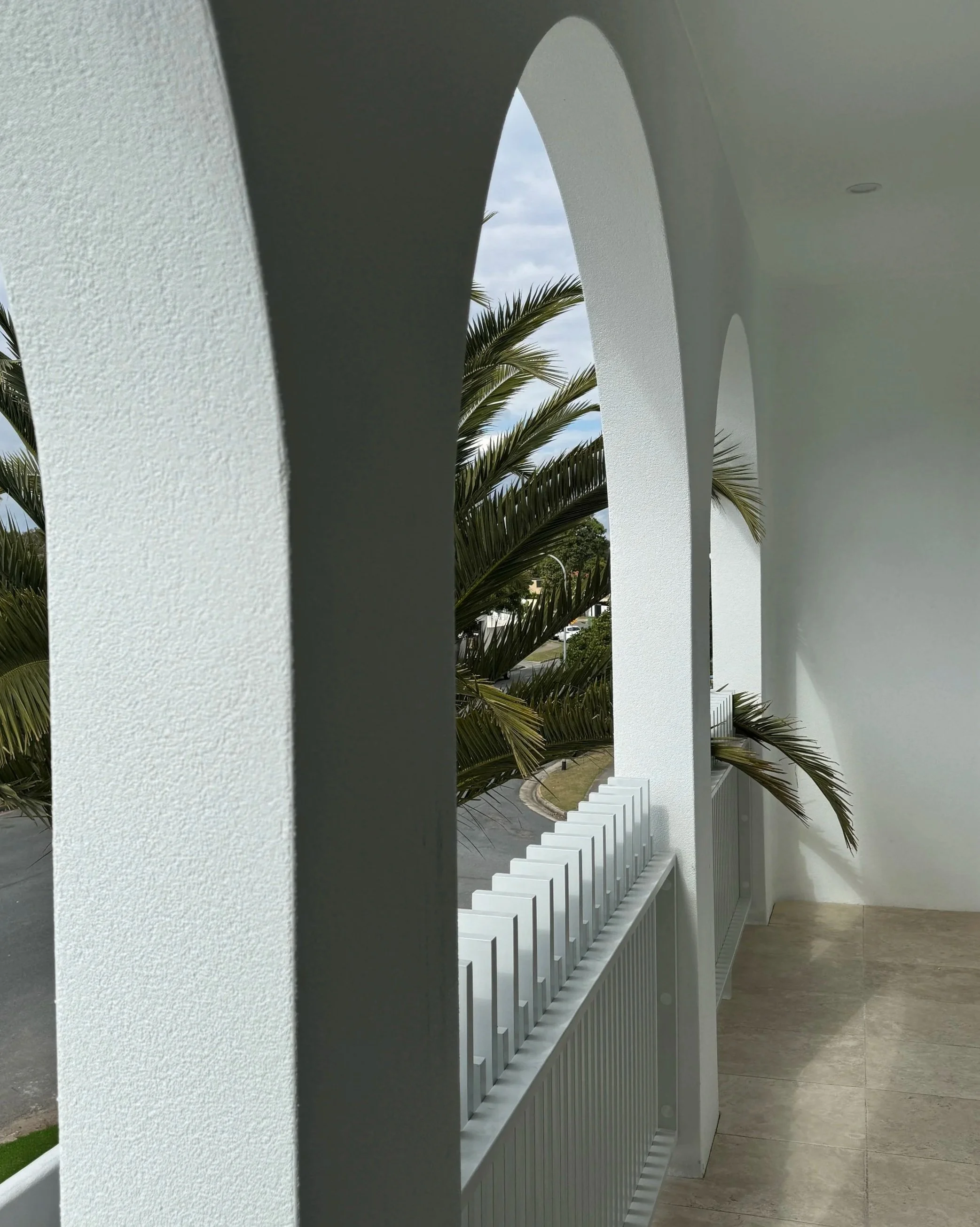 Balcony with white arches overlooking a street with palm trees.