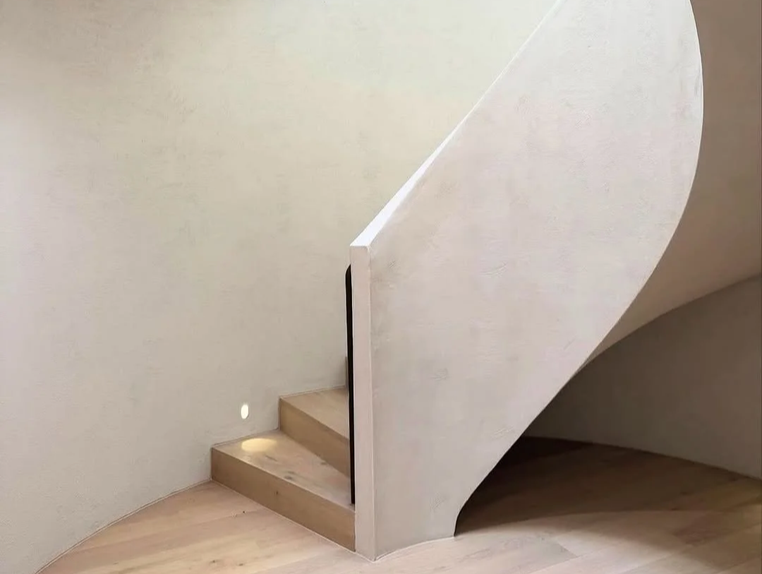 Close-up of a modern, minimalist staircase with curved white wall and light wooden steps, partially hidden beneath the arching wall.