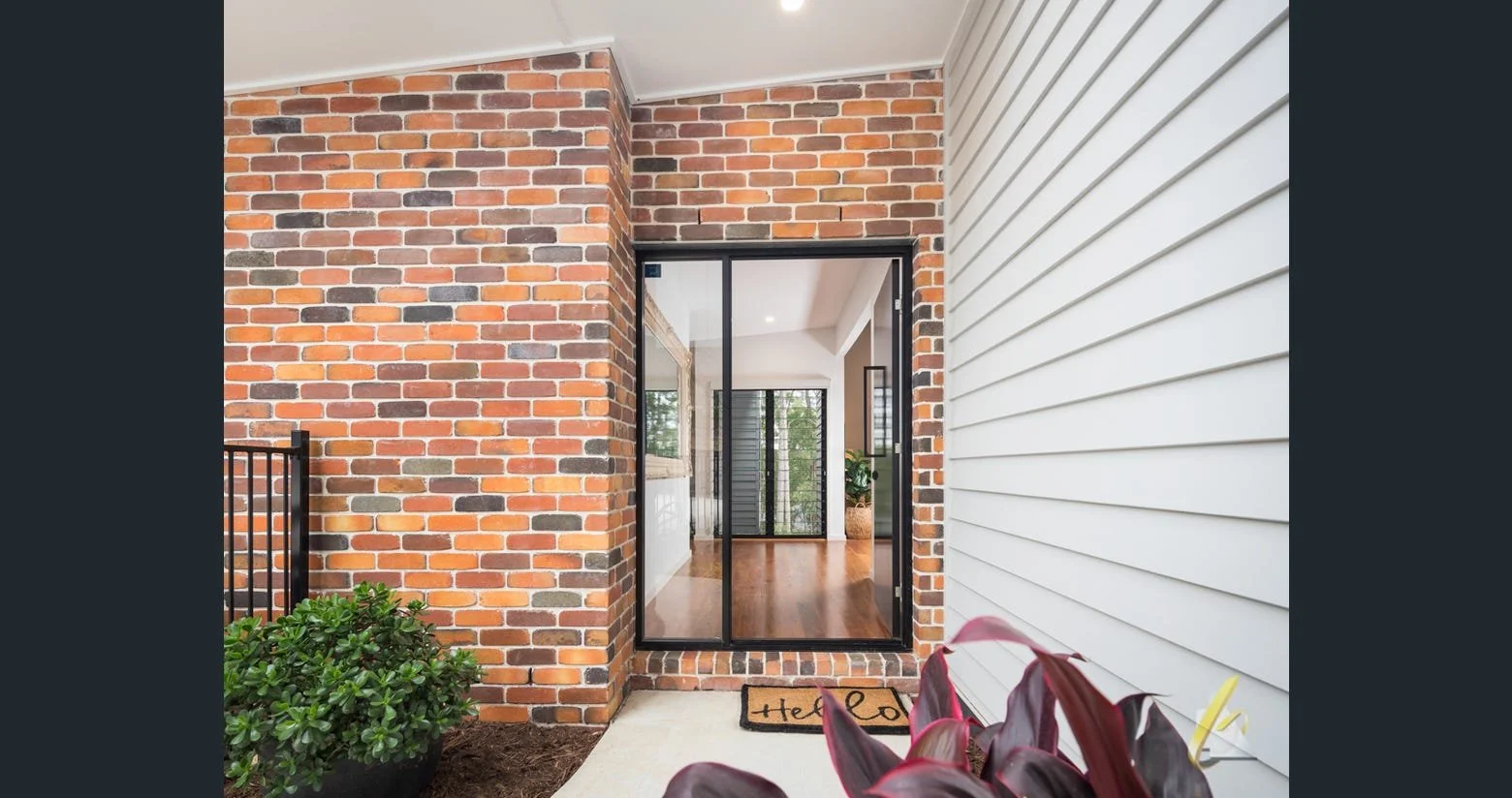 Welcoming home entrance featuring exposed brick wall, black-framed glass front door, and timber floorboards