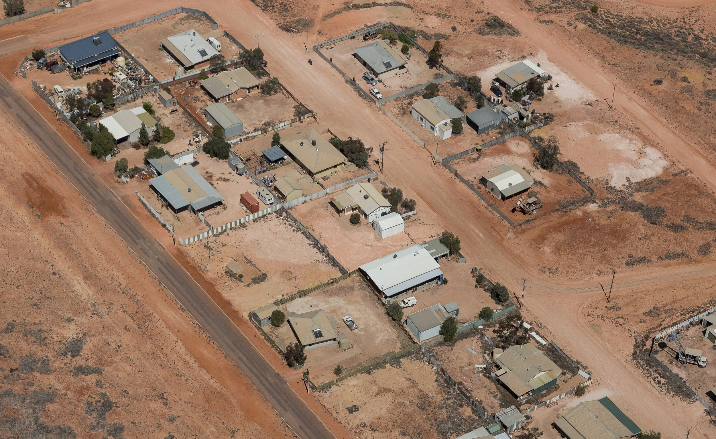 Aerial view of a rural residential area with dirt roads, fenced houses, and sparse vegetation in a desert landscape.
