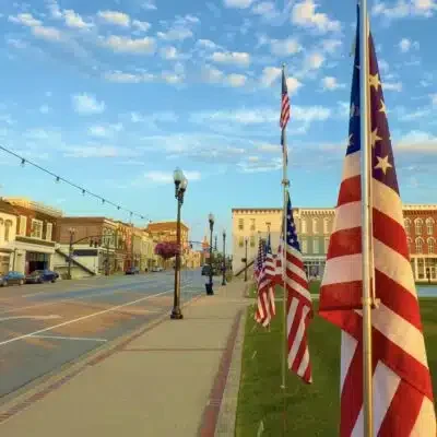 American flags lining a street with historic buildings and a clear sky.