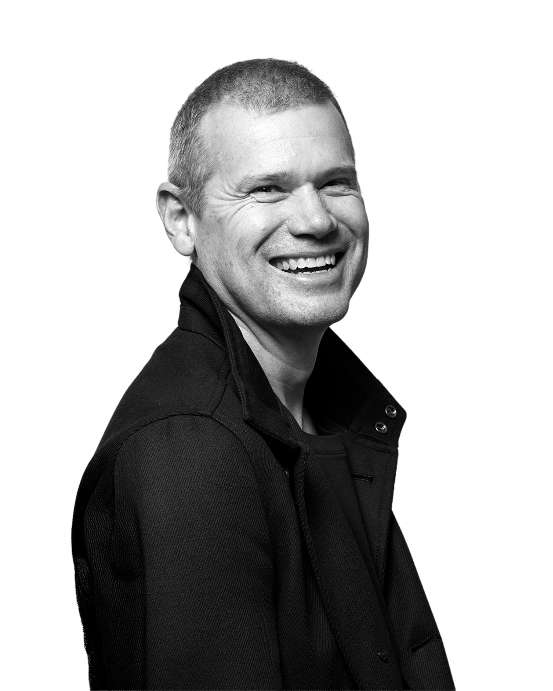 Black and white photo of a smiling man with short hair, wearing a dark jacket, against a black background.