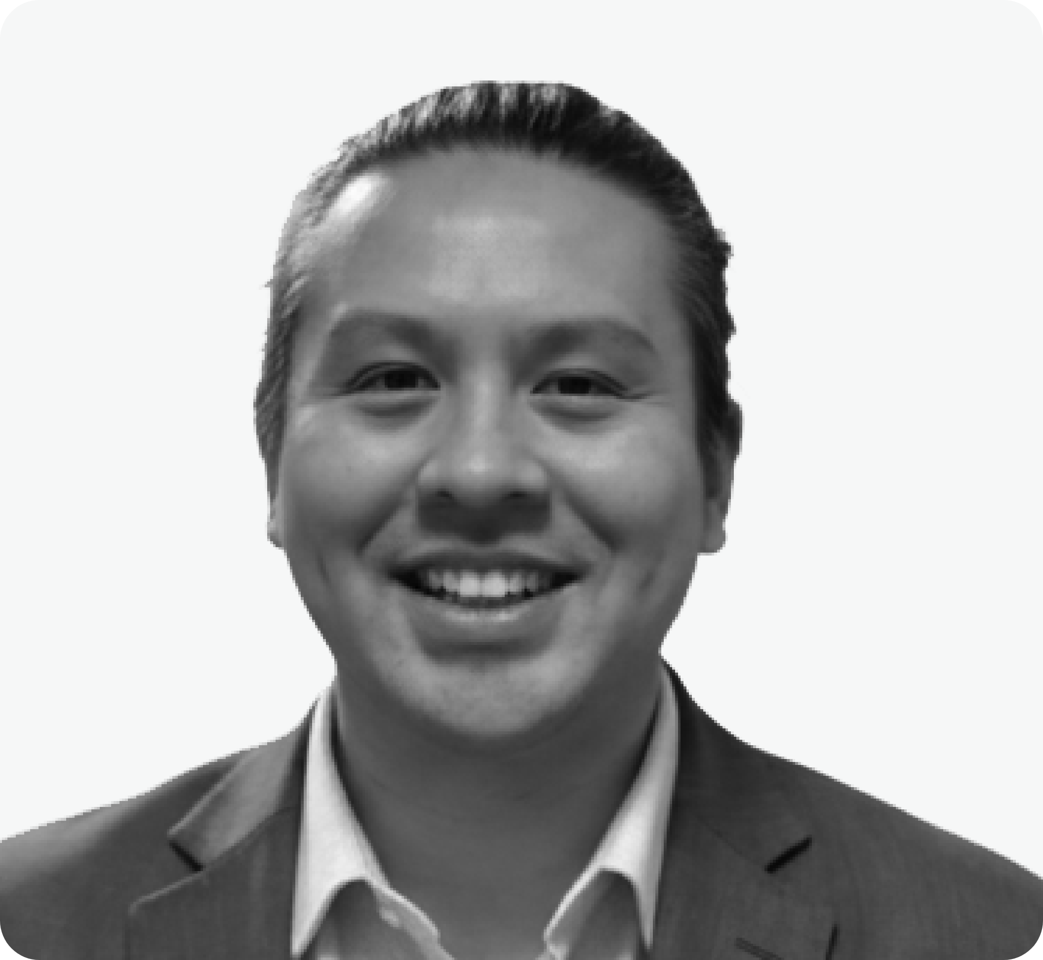 Black and white professional headshot of a smiling man with slicked-back hair, wearing a suit and dress shirt.