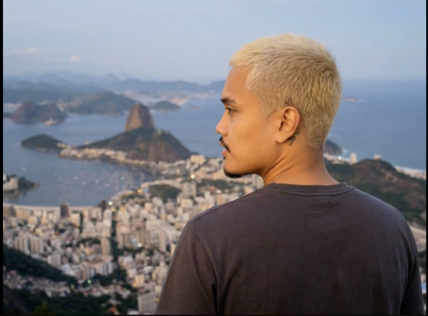 A man with blond hair looking over a cityscape of Rio de Janeiro, Brazil, including Sugarloaf Mountain and the bay.