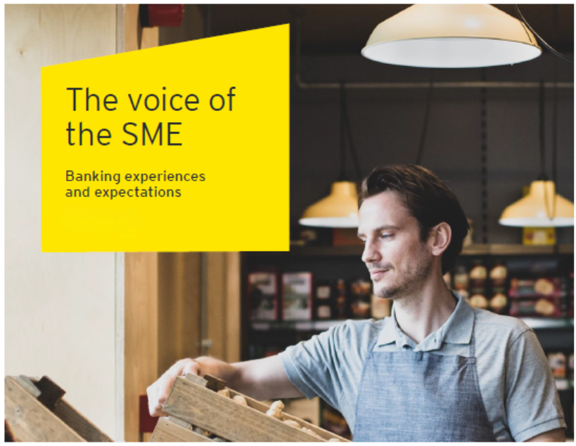 A man in a gray shirt working at a shop with wooden shelves and hanging lamps, with a yellow sign that reads 'The voice of the SME: Banking experiences and expectations.'