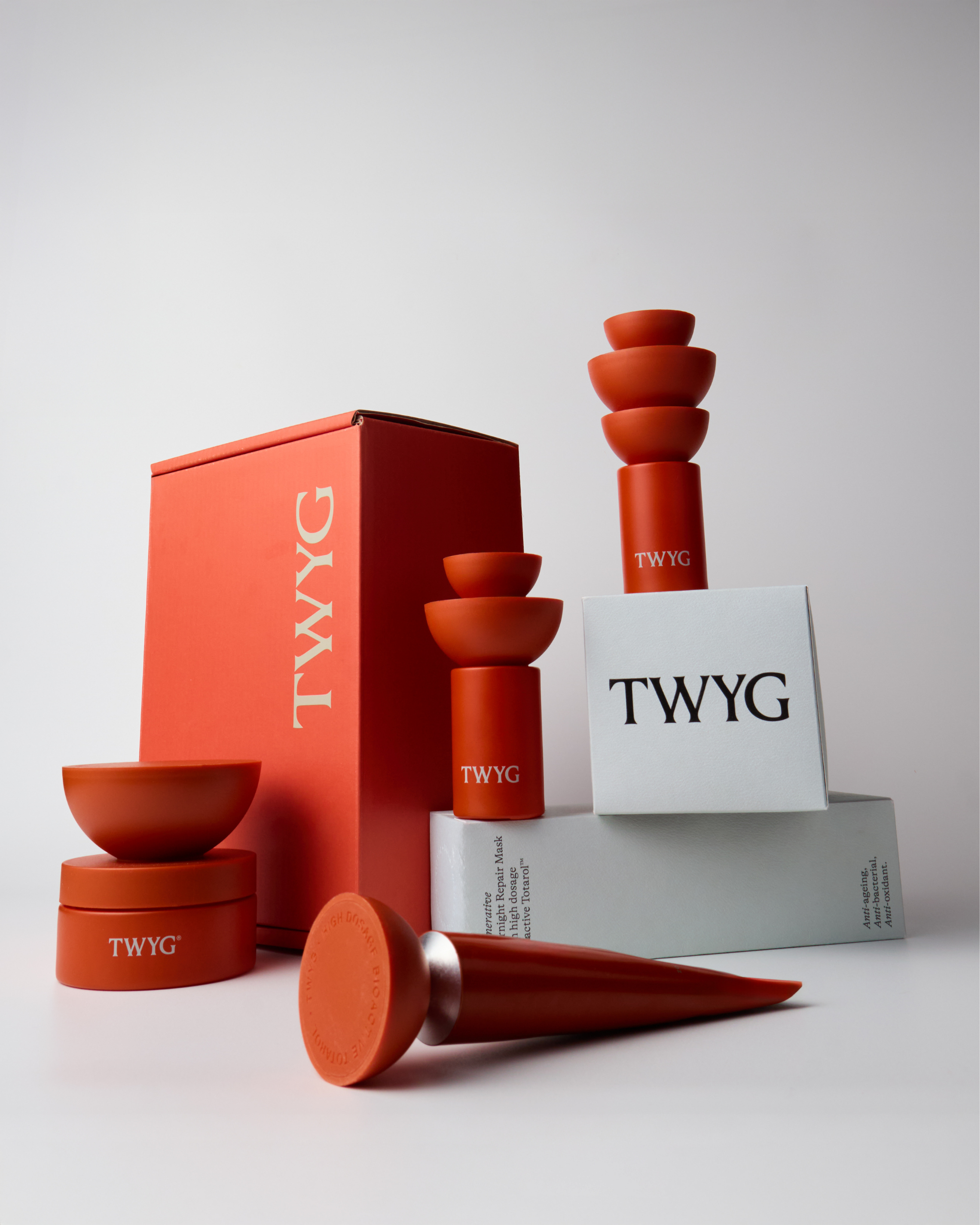 Collection of skincare products and containers with the brand name TWYG, including stacked bowls, boxes, and a tube, set against a plain background.