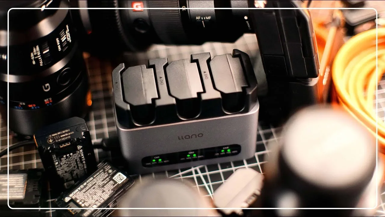 A camera gear setup on a wire mesh surface, including a camera lens, battery chargers, and various camera accessories.