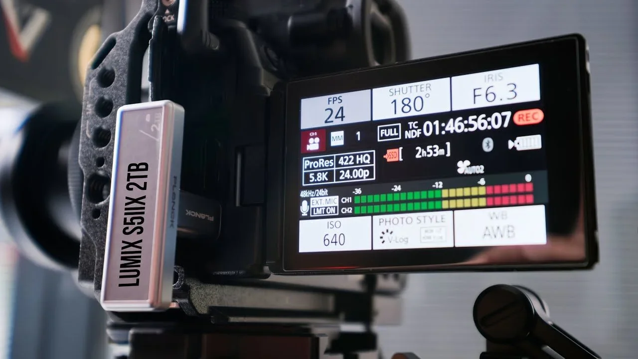 A professional video camera with a display screen showing camera settings and recording information.