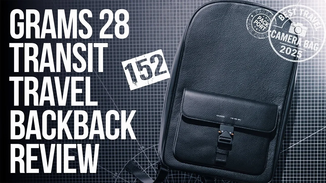 A black leather transit travel backpack on a graph paper background with white text reading 'Grams 28 Transit Travel Backpack Review' and a paper tag with the number 152. There are also circular stamps indicating 'Pack Port' and 'Camera Bag 2023'.