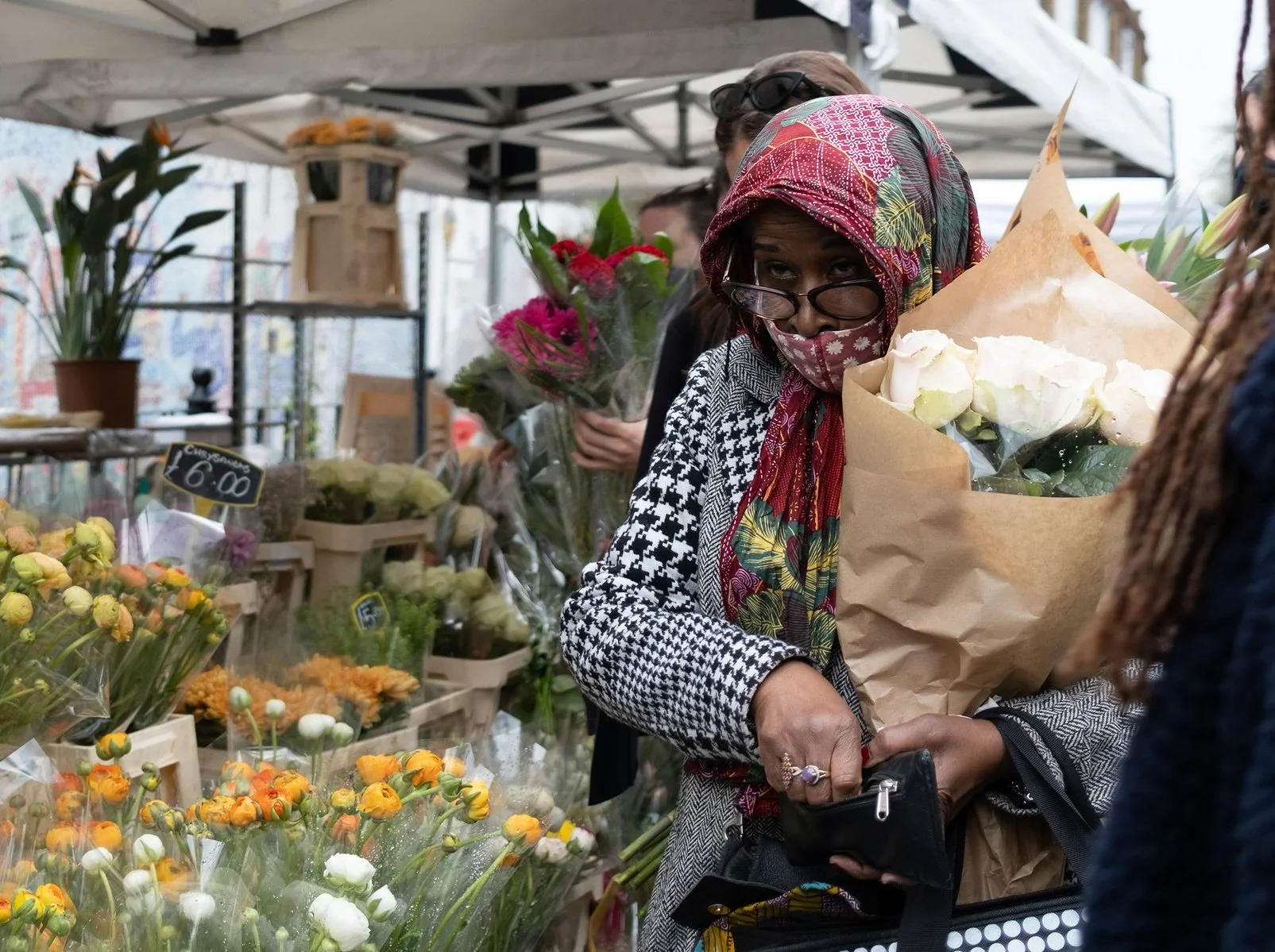 Woman holding and selecting flowers at a market stall, surrounded by various bouquets of colorful flowers, with a woman behind her also holding flowers.
