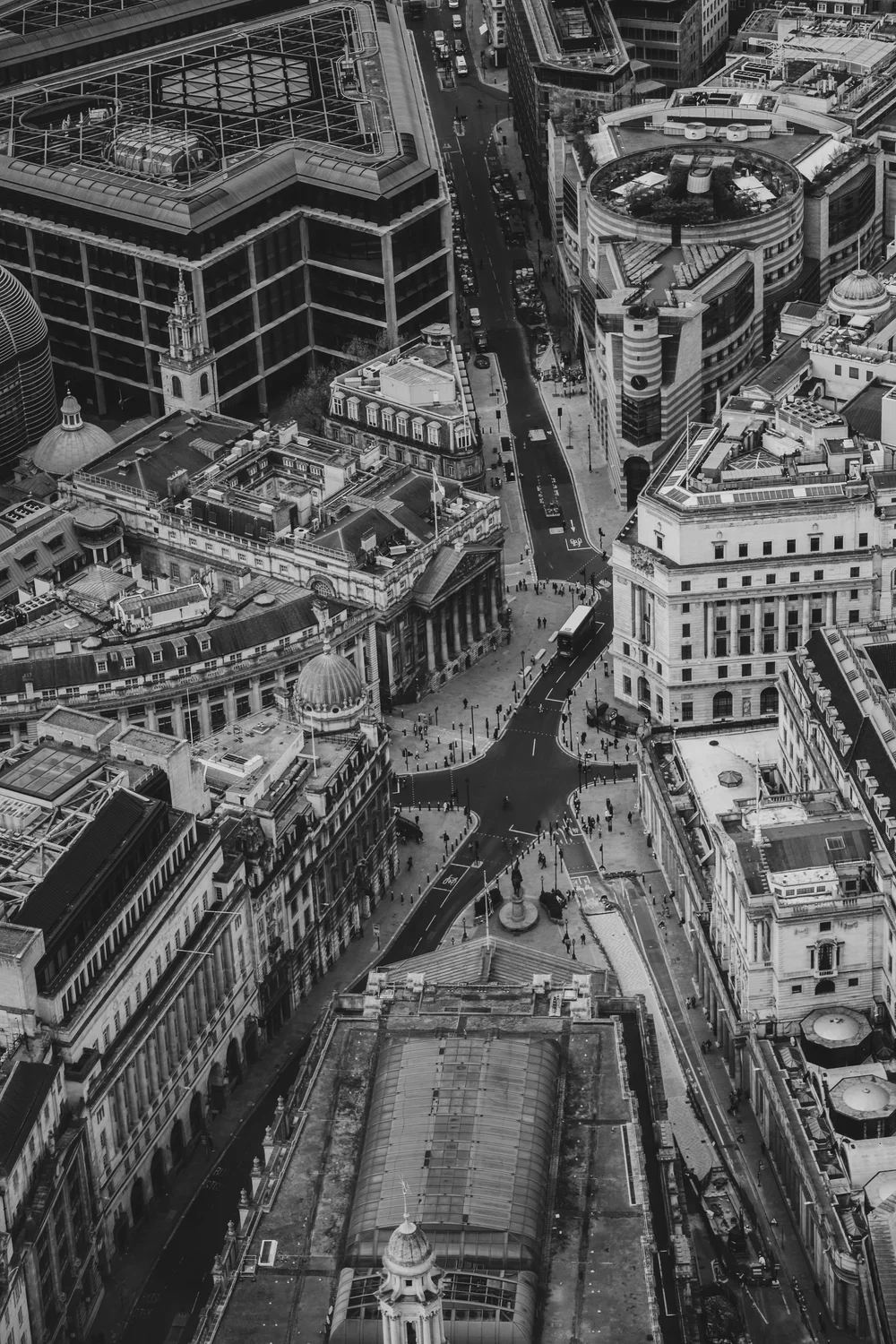 Aerial view of a city street with tall buildings, crowds of pedestrians, and vehicles, including buses, in a downtown area.