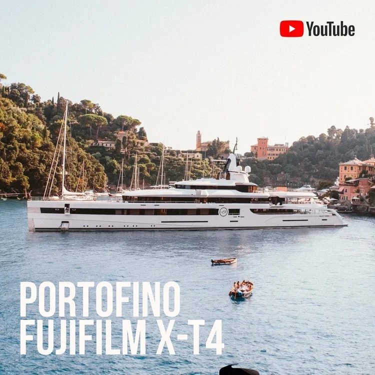 Large luxury yacht anchored in a harbor with hillside buildings in the background, featuring boats on the water and the YouTube logo in the top right corner, along with the text 'PORTOFINO FUDIFILM X-T4'.