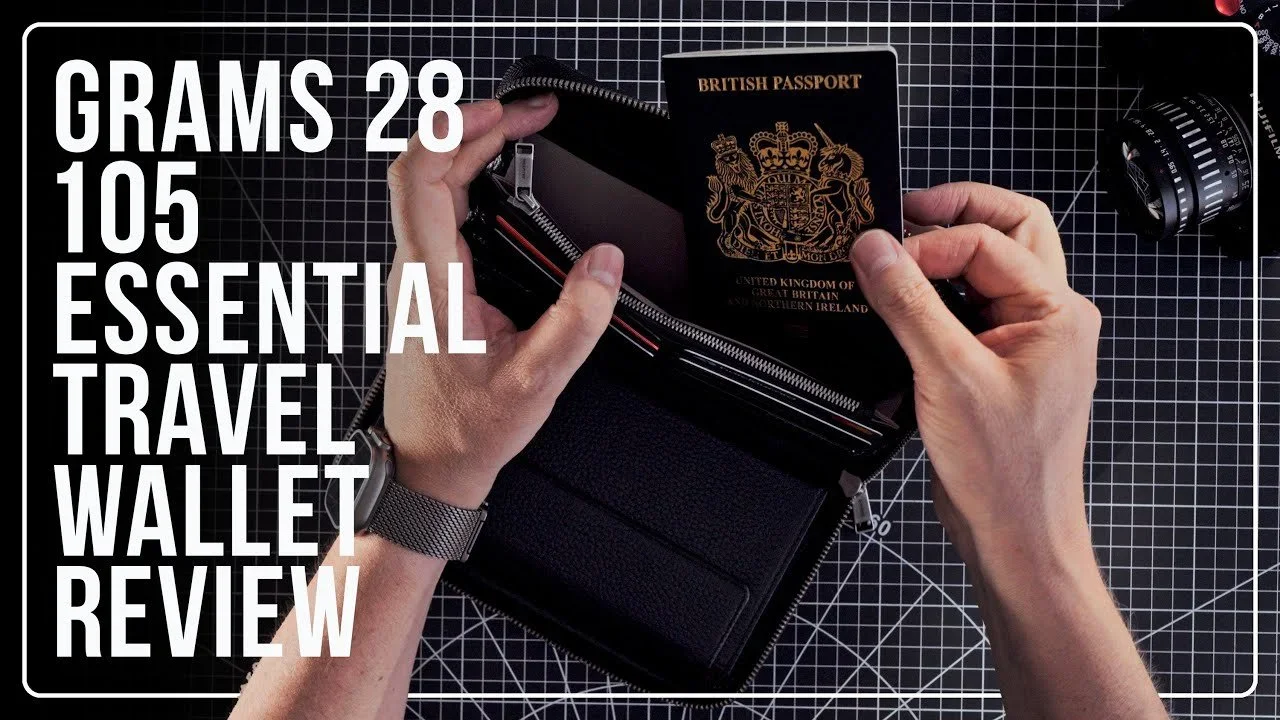 A travel wallet with a British passport placed inside, held open over a black grid cutting mat with a zipper compartment and a watch in the background, illustrating a review of essential travel wallet items.