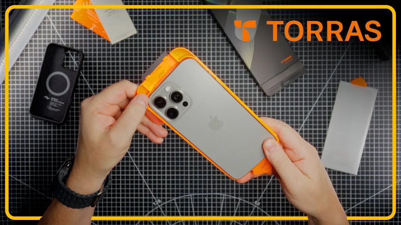 Person holding an iPhone with orange protective case, disassembled or in a repair kit, on a black grid work surface, with various electronic device parts around, including batteries and cases, and a Torras logo in the top right corner.