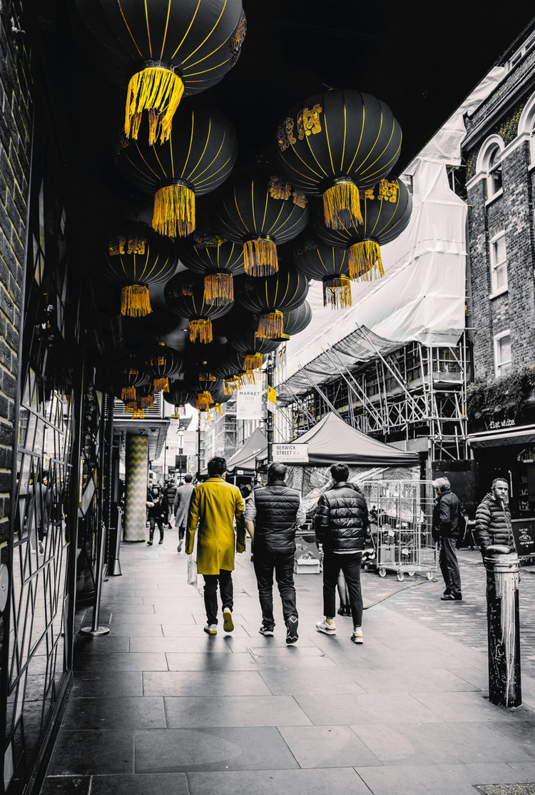Street scene with people walking under a canopy of black lanterns with yellow tassels in a city.