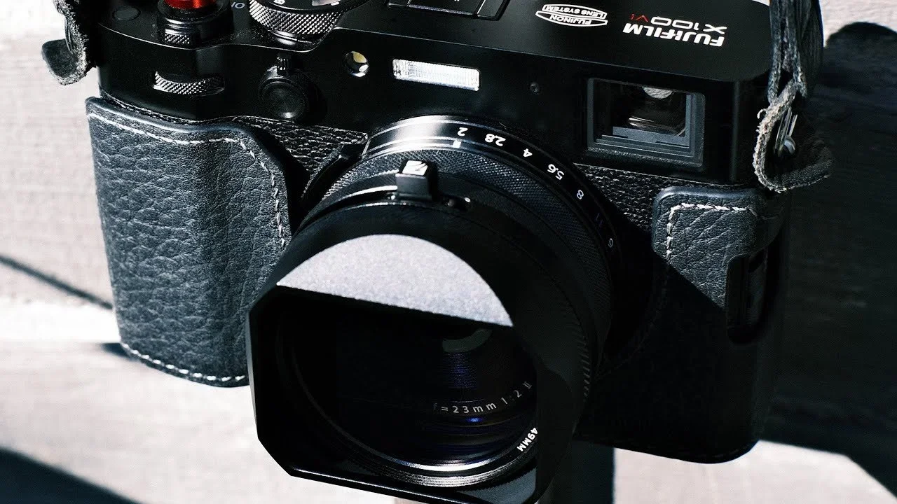 Close-up of a vintage black Fujifilm camera with a 23mm lens, mounted on a strap, resting on a surface.