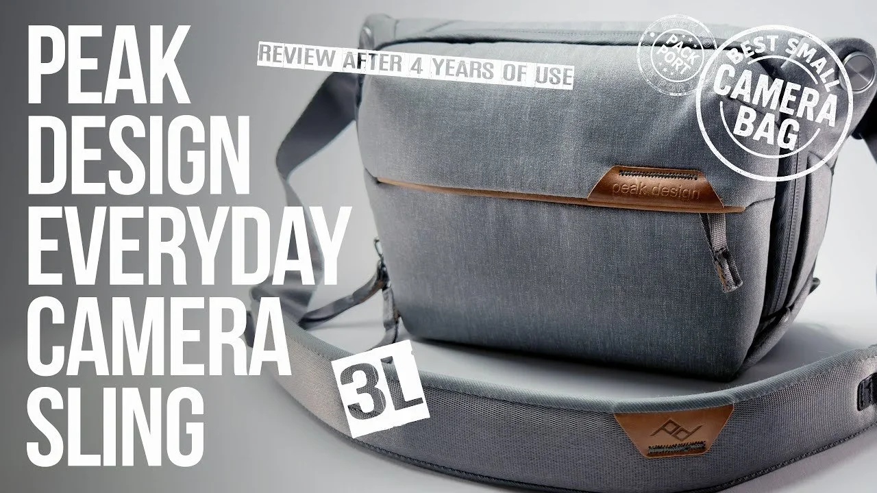 Gray camera bag with leather accents and straps, and a detachable sling strap, positioned on a light gray surface with large white text and branded labels overlapping the bag.