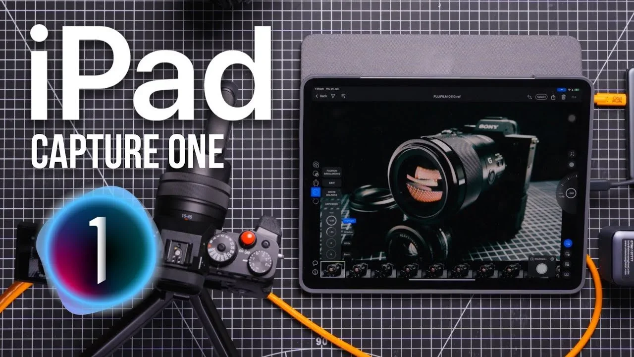 An iPad displaying a camera app with a camera lens on the screen, placed on a black grid surface with various camera and tech accessories surrounding it.