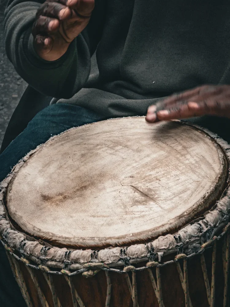 A person playing a traditional drum with a wooden top and a woven exterior.