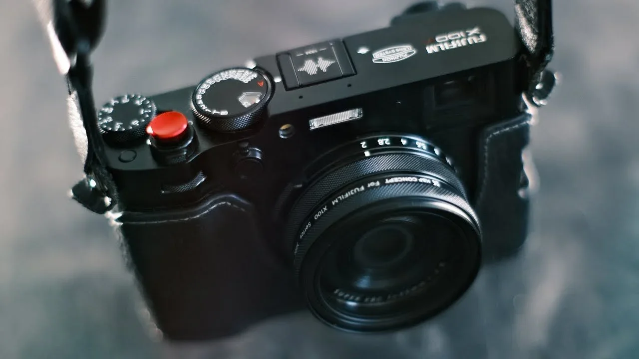 A black compact camera with a large lens and red shutter button, placed on a dark surface.