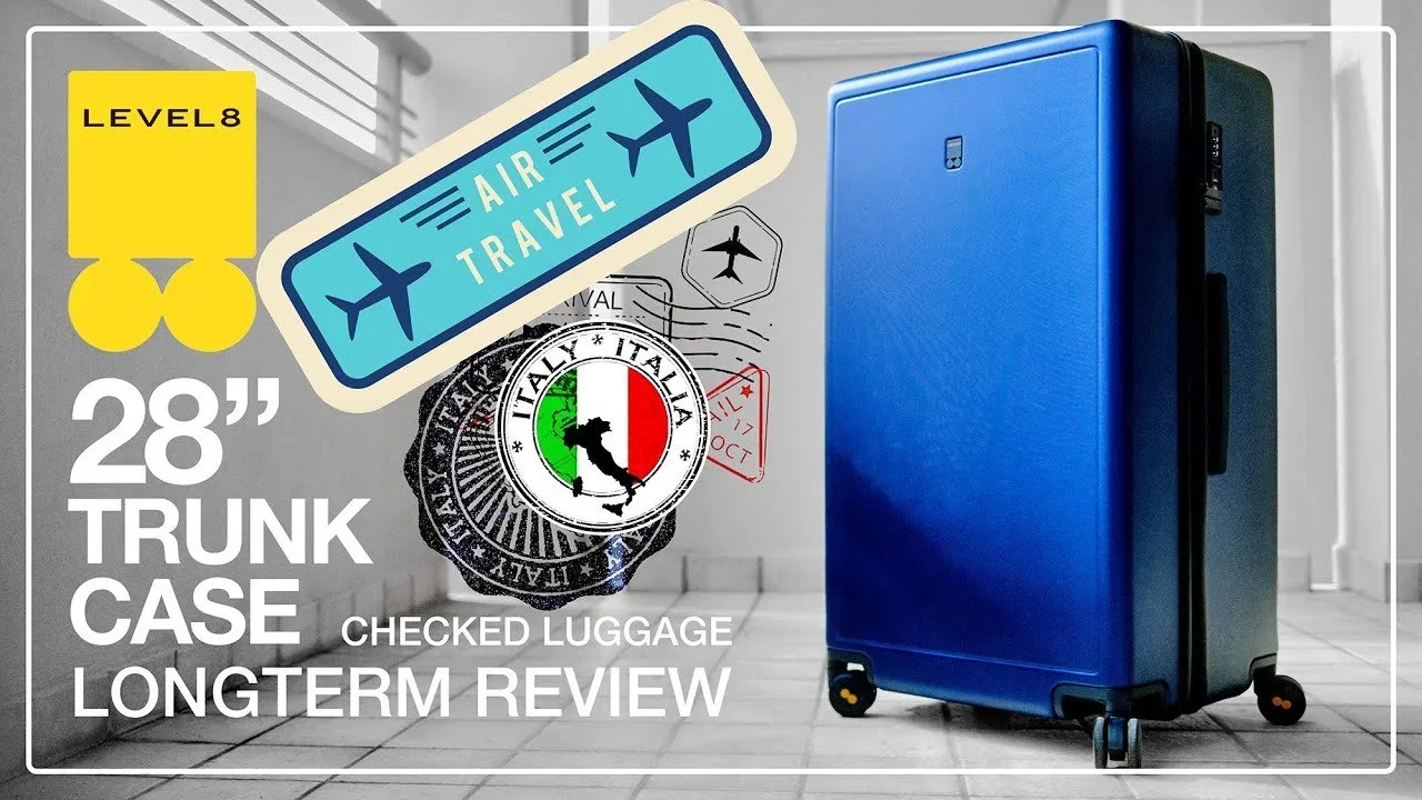 Image of a blue 28-inch trunk suitcase, with various travel related stickers and labels on the wall in the background, including an Italian emblem, airplane tickets, and travel icons.