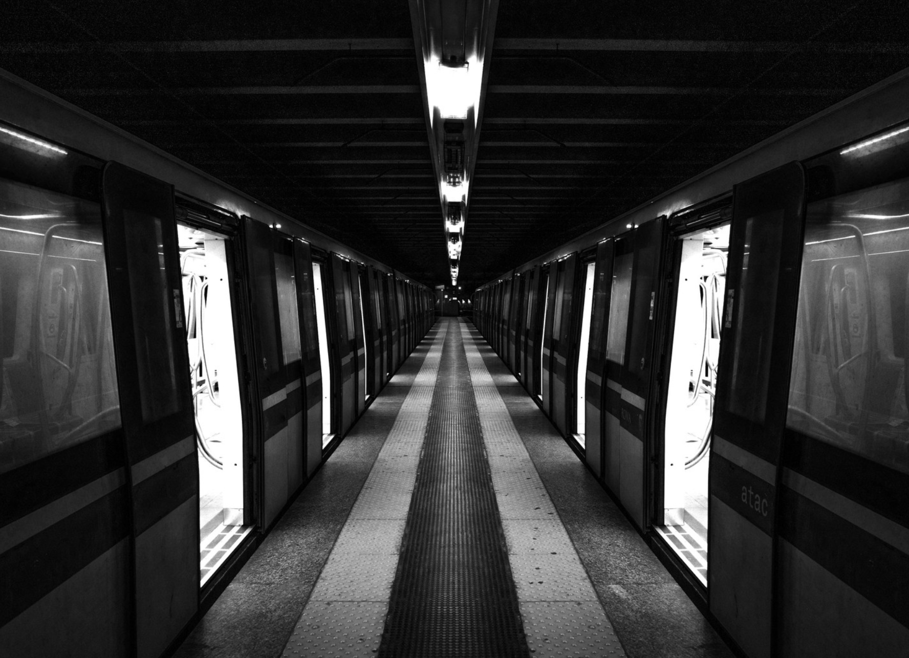 Empty subway platform with closed train doors on both sides, dim lighting, and a dark ceiling.