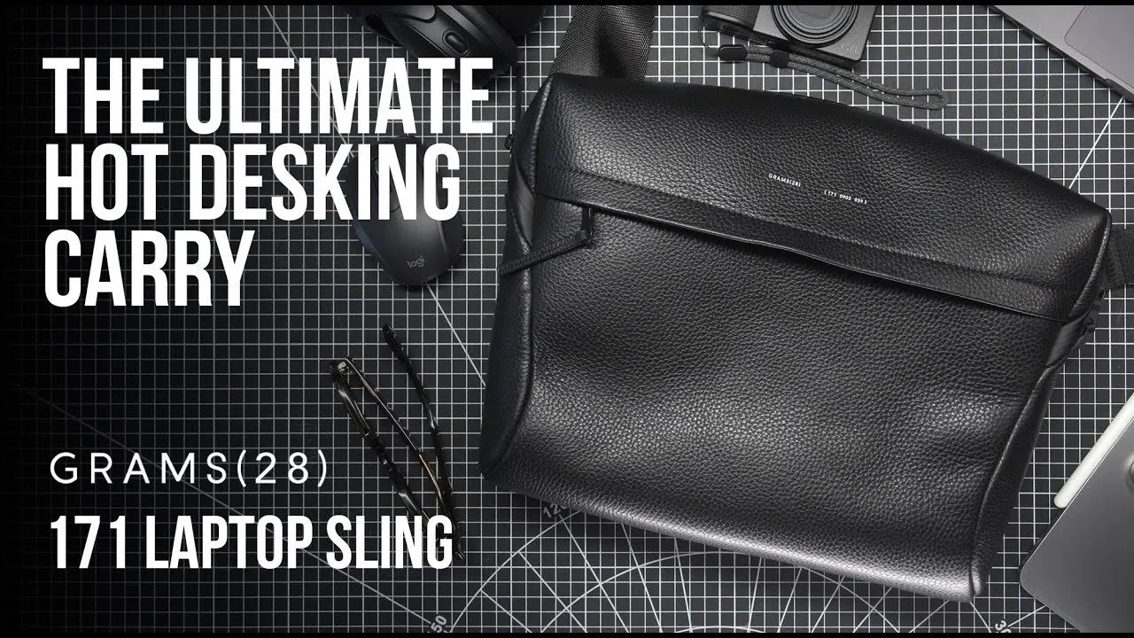 A black leather laptop sleeve, a computer mouse, a pair of glasses, a stylus, and part of a laptop are arranged on a black grid cutting mat, with white text overlay reading "The Ultimate Hot Deskin Carry, Grams(28), 171 Laptop Sling."