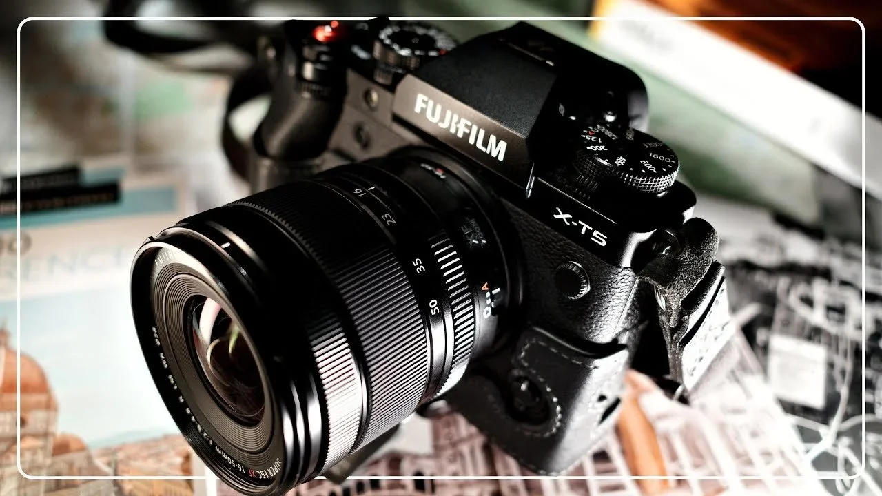 A Fujifilm X-T5 camera with a large zoom lens mounted on it, placed on a surface with printed images or maps.
