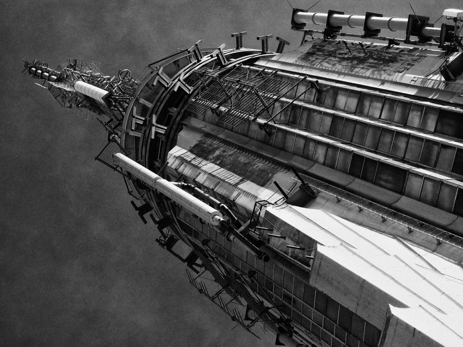 Black and white photo of an upward-looking view of a tall, modern skyscraper with a curved design and various architectural features.